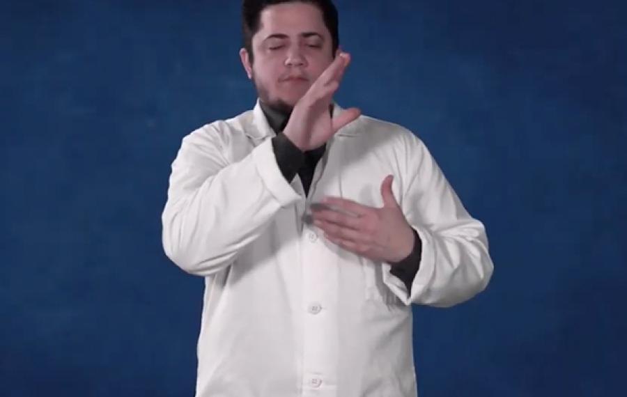 A male in a white medical coat standing in front of a dark blue background.