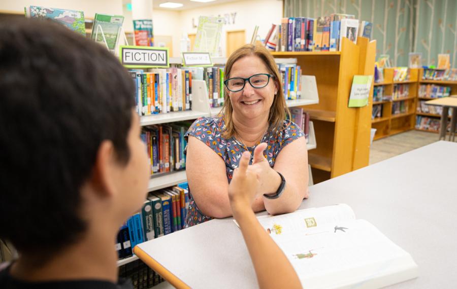 A Teacher of the Deaf sits across from a student at a table. They are both using ASL