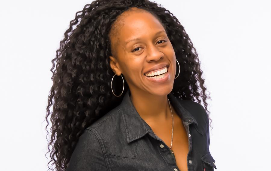A Black woman with long dark hair smiling at the camera. She is wearing a dark button down shirt.