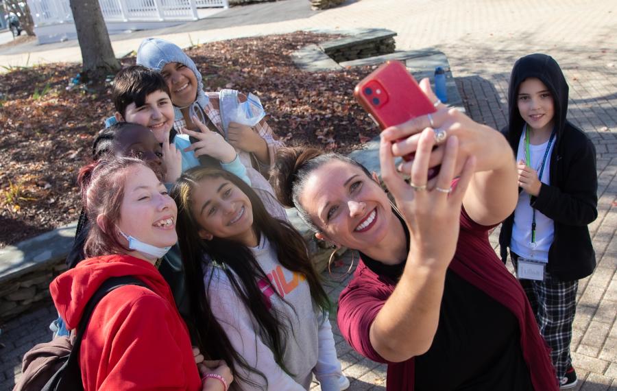 A group of students with Renca Dunn. Renca is holding up a phone and taking a selfie with the group.