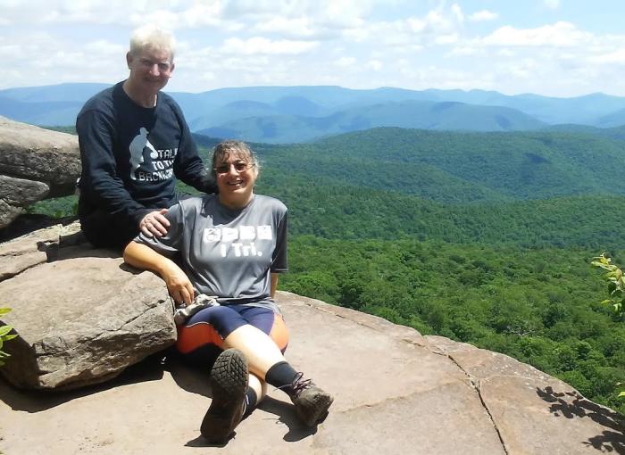 Two individuals sitting on rocks overlooking a large landscape.