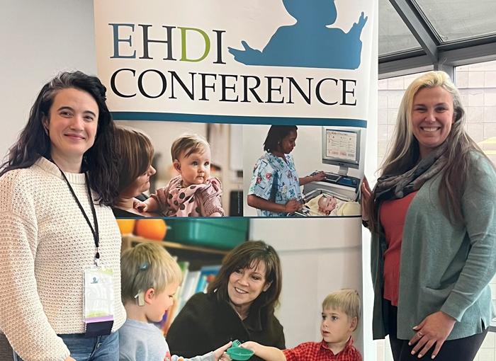 Claire Miller and Thea Cabral stand next to an EHDI Conference Banner.