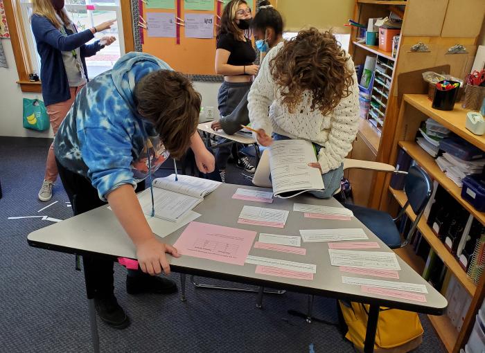 Two students are standing over a desk in a classroom doing work.