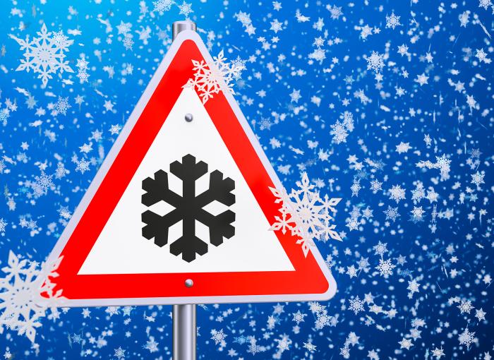 A bright blue background with snowflakes. Foreground: A Triangle sign with red outline, white background and one black snowflake.