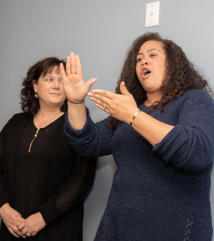 Two females stand side by side. The female on the right is signing.