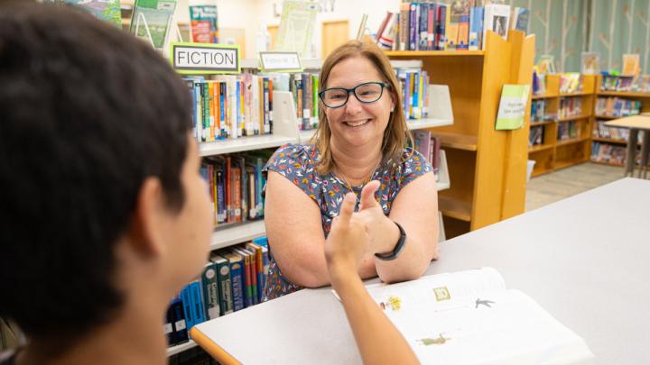 A Teacher of the Deaf sits across from a student at a table. They are both using ASL