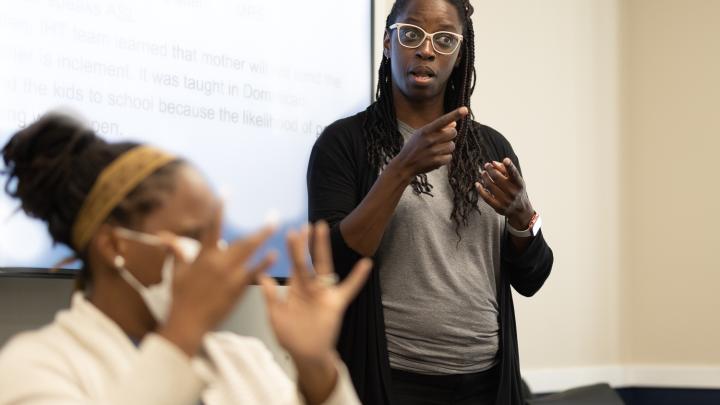 A female Black Deaf Interpreter is focused in the background. 