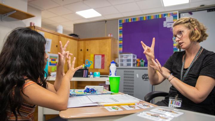 A teacher of the deaf and a student sitting across the table from one another.