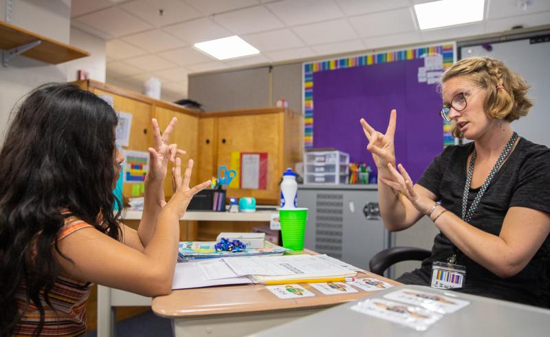 A teacher of the deaf and a student sitting across the table from one another.