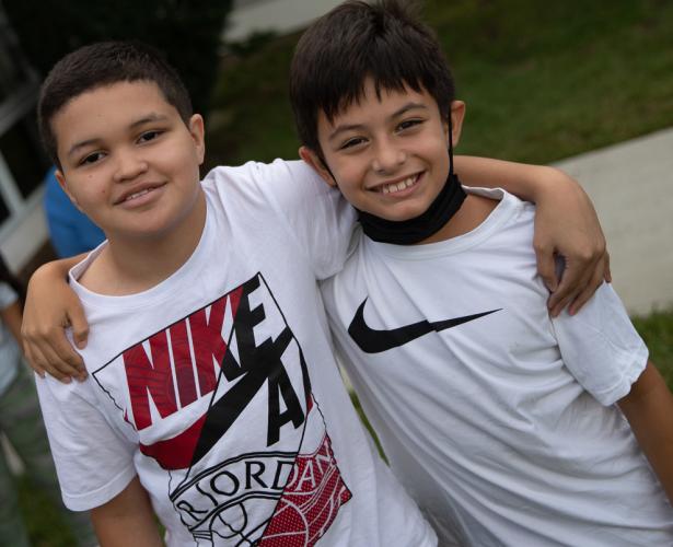 Two boys are standing with their arms around each other's shoulders.