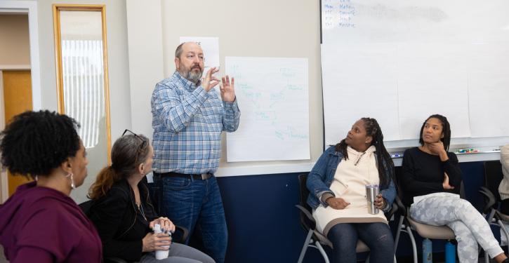 White man with blue button up shirt presenting to staff