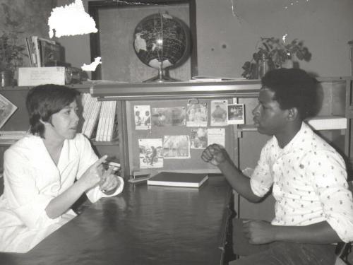 Maureen O'Donnell is sitting across the table from a Black man. they are both wearing white shirts.