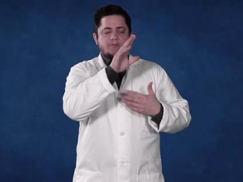 A male in a white medical coat standing in front of a dark blue background.