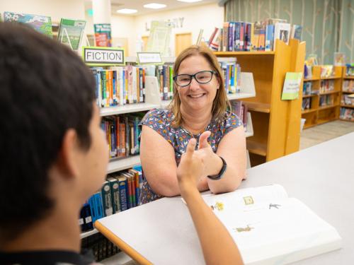 A Teacher of the Deaf sits across from a student at a table. They are both using ASL