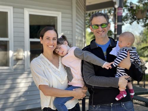 A family of four is smiling together outside.