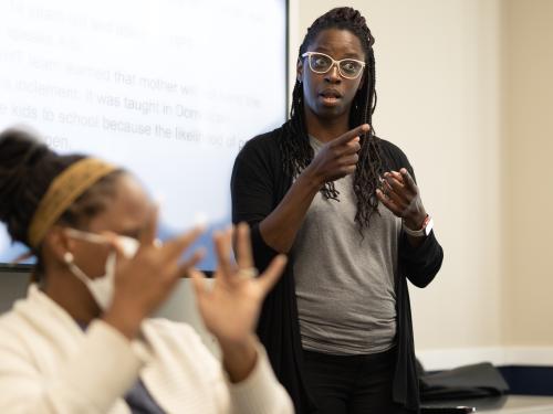 A female Black Deaf Interpreter is focused in the background. 