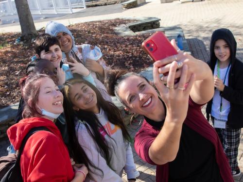 A group of students with Renca Dunn. Renca is holding up a phone and taking a selfie with the group.