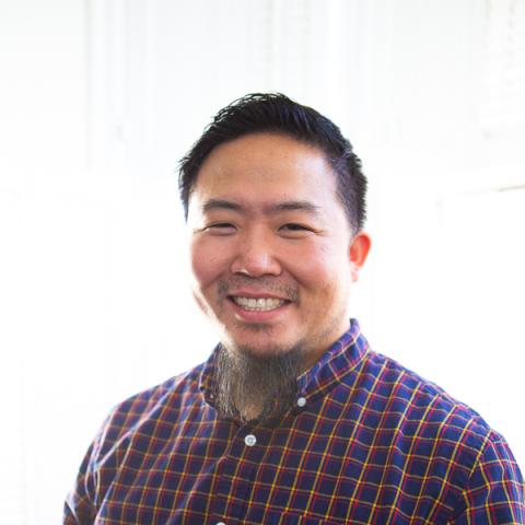 A male with short dark hair and a button down shirt. White background.