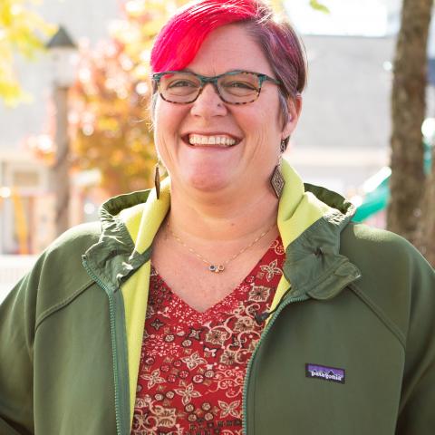 A white woman with short red hair and glasses standing outside in a green jacket.