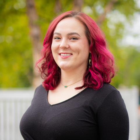 A white woman standing outside. Medium length red hair and a black long sleeved shirt.