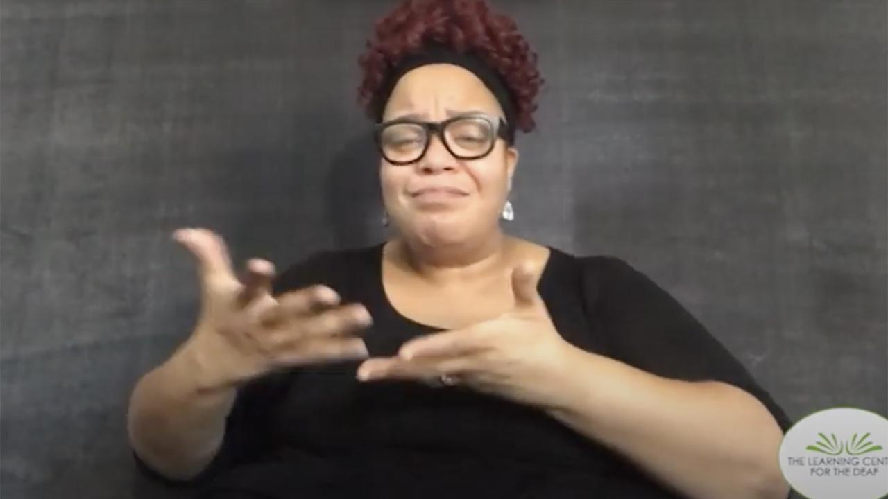 A Black woman in front of a gray screen, in a black shirt, explaining the TLC Racial Equity Plan.